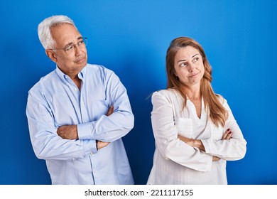 Middle Age Hispanic Couple Standing Over Blue Background Looking To The Side With Arms Crossed Convinced And Confident 