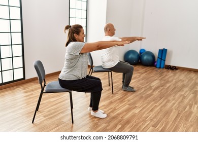 Middle age hispanic couple stretching using chair at sport center. - Powered by Shutterstock