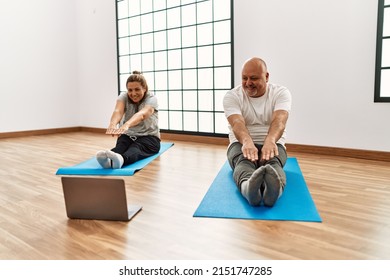 Middle Age Hispanic Couple Stretching Having Online Sport Class Using Laptop At Gym