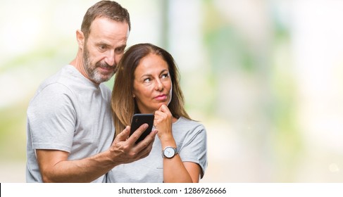 Middle Age Hispanic Couple Texting Message On Smartphone Ver Isolated Background Serious Face Thinking About Question, Very Confused Idea