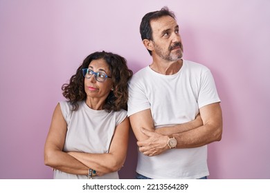 Middle Age Hispanic Couple Together Over Pink Background Looking To The Side With Arms Crossed Convinced And Confident 