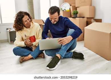 Middle Age Hispanic Couple Using Laptop And Drinking Coffee. Sitting On The Floor With Dog At New Home.