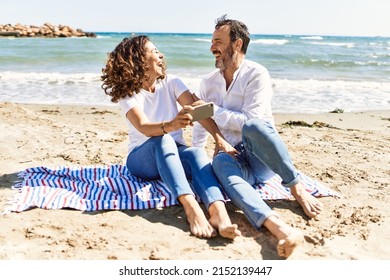 Middle age hispanic couple using smartphone sitting on the towel at the beach. - Powered by Shutterstock