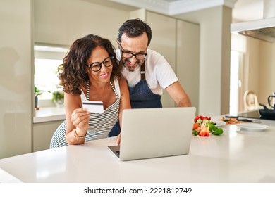 Middle Age Hispanic Couple Using Laptop And Credit Card At Kitchen