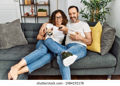 Middle age hispanic couple watching movie and eating popcorn sitting on the sofa at home.
