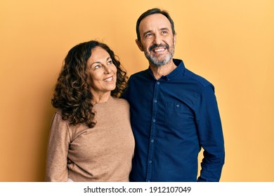 Middle age hispanic couple wearing casual clothes smiling looking to the side and staring away thinking. 