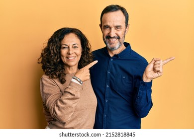 Middle age hispanic couple wearing casual clothes cheerful with a smile on face pointing with hand and finger up to the side with happy and natural expression 
