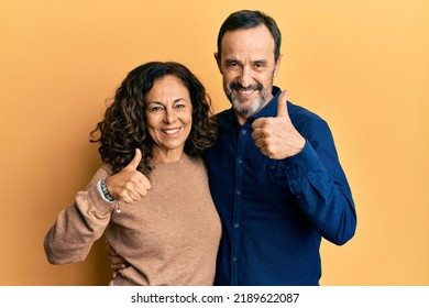 Middle age hispanic couple wearing casual clothes doing happy thumbs up gesture with hand. approving expression looking at the camera showing success.  - Powered by Shutterstock