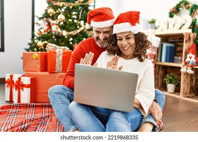 Middle age hispanic couple wearing christmas hat. Sitting on the floor having video call using laptop at home. - Powered by Shutterstock