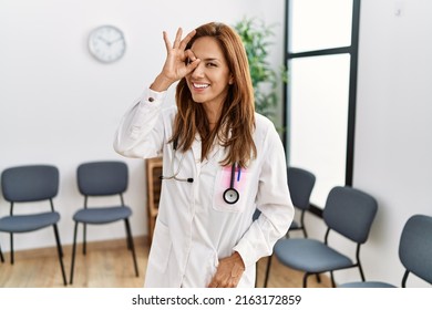 Middle Age Hispanic Doctor Woman At Waiting Room Smiling Happy Doing Ok Sign With Hand On Eye Looking Through Fingers 