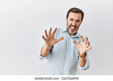 Middle age hispanic man with beard standing over isolated background afraid and terrified with fear expression stop gesture with hands, shouting in shock. panic concept. 