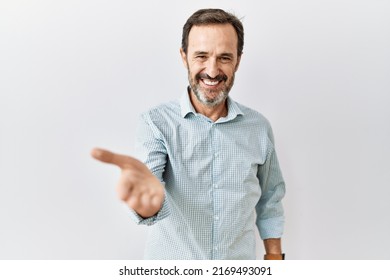 Middle age hispanic man with beard standing over isolated background smiling cheerful offering palm hand giving assistance and acceptance.  - Powered by Shutterstock