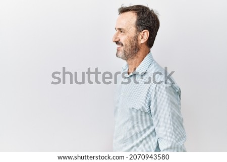 Middle age hispanic man with beard standing over isolated background looking to side, relax profile pose with natural face and confident smile. 