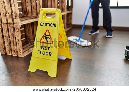Middle age hispanic man cleaning floor with caution wet floor banner at home