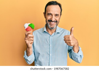 Middle Age Hispanic Man Holding Ice Cream Smiling Happy And Positive, Thumb Up Doing Excellent And Approval Sign 