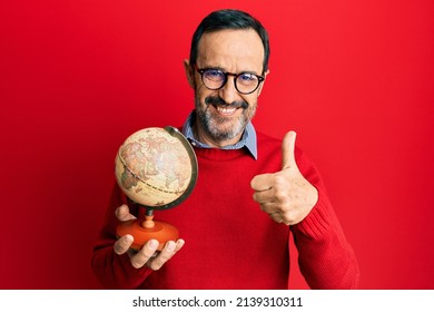 Middle age hispanic man holding vintage world ball smiling happy and positive, thumb up doing excellent and approval sign 