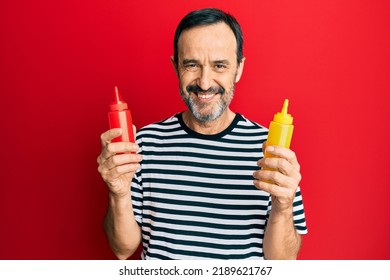 Middle Age Hispanic Man Holding Ketchup And Mustard Bottle Smiling With A Happy And Cool Smile On Face. Showing Teeth. 