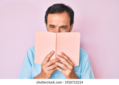 Middle Age Hispanic Man Reading Book Smiling And Laughing Hard Out Loud Because Funny Crazy Joke. 