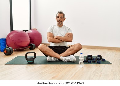 Middle Age Hispanic Man Sitting On Training Mat At The Gym Happy Face Smiling With Crossed Arms Looking At The Camera. Positive Person. 