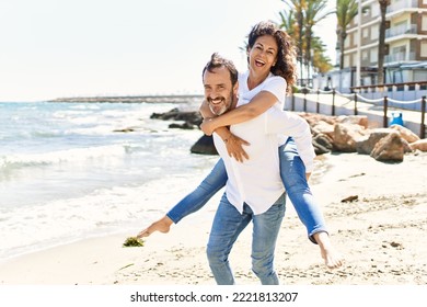 Middle age hispanic man smiling happy holding woman on his back at the beach. - Powered by Shutterstock