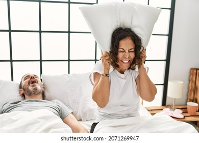 Middle Age Hispanic Man Snoring And Woman Angry Covering Ears With Pillow At Bedroom.