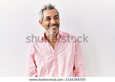 Middle age hispanic man standing over isolated background looking away to side with smile on face, natural expression. laughing confident. 