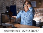 Middle age hispanic man using touchpad sitting on the table at night surprised with hand on head for mistake, remember error. forgot, bad memory concept. 