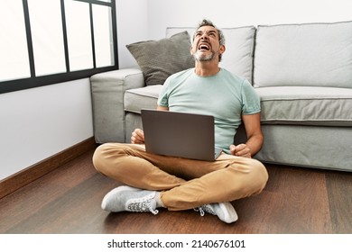 Middle age hispanic man using laptop sitting on the floor at the living room angry and mad screaming frustrated and furious, shouting with anger. rage and aggressive concept.  - Shutterstock ID 2140676101