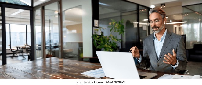 Middle age hispanic man using computer remote for business studying, watching online virtual webinar training meeting, video call. Mature businessman talking on laptop in office. Banner, copy space