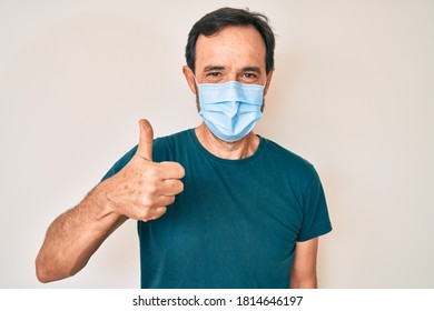 Middle age hispanic man wearing medical mask smiling happy and positive, thumb up doing excellent and approval sign 