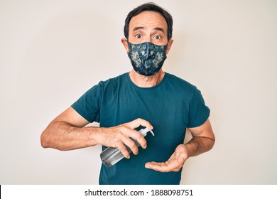 Middle Age Hispanic Man Wearing Covid-19 Protection Mask Using Hand Sanitizer Gel Puffing Cheeks With Funny Face. Mouth Inflated With Air, Catching Air. 