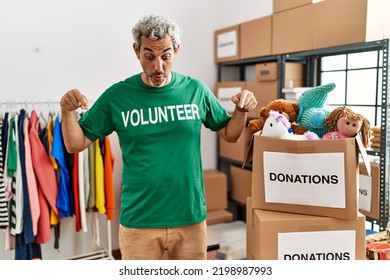 Middle Age Hispanic Man Wearing Volunteer T Shirt At Donations Stand Pointing Down With Fingers Showing Advertisement, Surprised Face And Open Mouth 