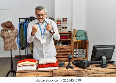 Middle age hispanic man working as manager at retail boutique angry and mad raising fists frustrated and furious while shouting with anger. rage and aggressive concept. 