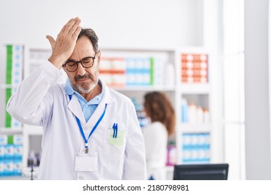 Middle age hispanic man working at pharmacy drugstore surprised with hand on head for mistake, remember error. forgot, bad memory concept. 