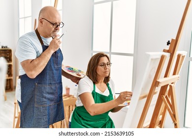 Middle Age Hispanic Painter Couple With Serious Expression Painting At Art Studio.