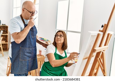 Middle Age Hispanic Painter Couple With Serious Expression Painting At Art Studio.