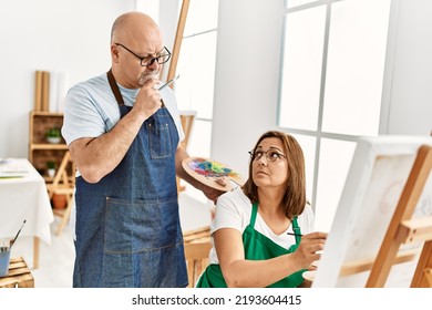 Middle Age Hispanic Painter Couple With Serious Expression Painting At Art Studio.