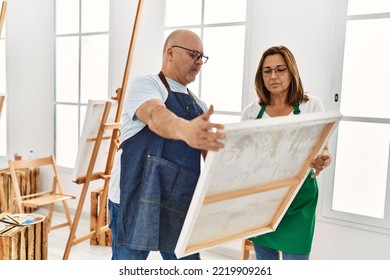Middle Age Hispanic Painter Couple With Serious Expression Looking Canvas At Art Studio.