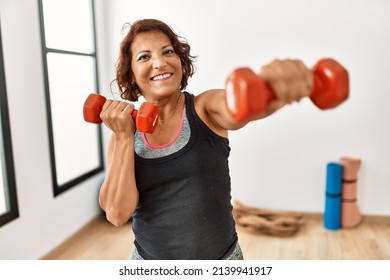 Middle age hispanic sporty woman smiling happy training using dumbbells at sport center. - Powered by Shutterstock