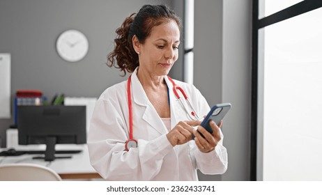 Middle age hispanic woman doctor using smartphone at clinic - Powered by Shutterstock