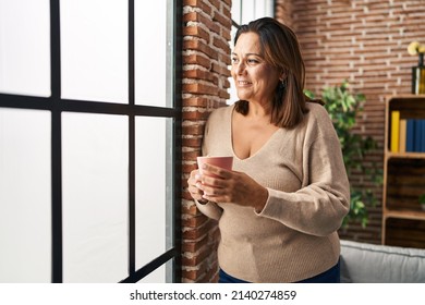 Middle age hispanic woman drinking coffee standing at home - Powered by Shutterstock