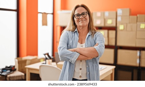 Middle age hispanic woman ecommerce business worker standing with arms crossed gesture smiling at office - Powered by Shutterstock