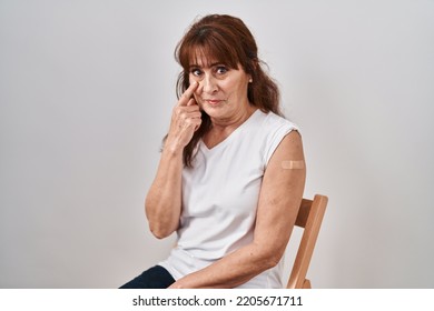 Middle Age Hispanic Woman Getting Vaccine Showing Arm With Band Aid Pointing To The Eye Watching You Gesture, Suspicious Expression 