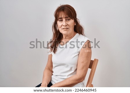 Middle age hispanic woman getting vaccine showing arm with band aid looking sleepy and tired, exhausted for fatigue and hangover, lazy eyes in the morning. 
