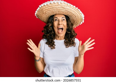 Middle Age Hispanic Woman Holding Mexican Hat Celebrating Mad And Crazy For Success With Arms Raised And Closed Eyes Screaming Excited. Winner Concept 