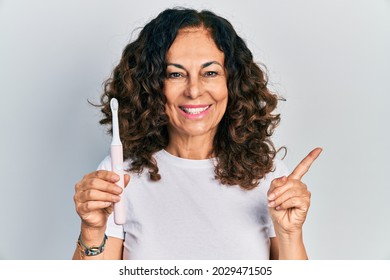 Middle Age Hispanic Woman Holding Electric Toothbrush Smiling Happy Pointing With Hand And Finger To The Side 