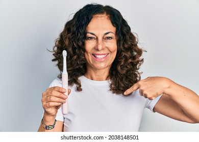 Middle Age Hispanic Woman Holding Electric Toothbrush Pointing Finger To One Self Smiling Happy And Proud 