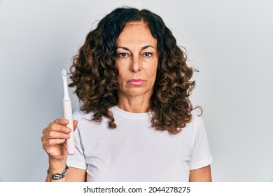 Middle Age Hispanic Woman Holding Electric Toothbrush Thinking Attitude And Sober Expression Looking Self Confident 