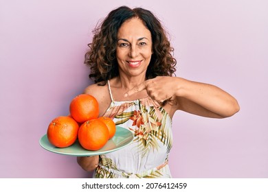 Middle Age Hispanic Woman Holding Plate With Fresh Oranges Smiling Happy Pointing With Hand And Finger 