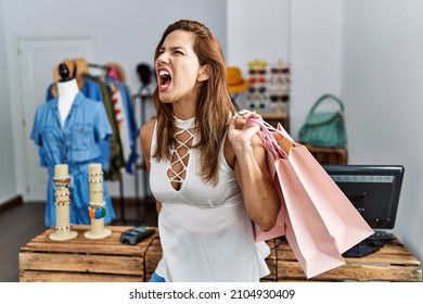 Middle Age Hispanic Woman Holding Shopping Bags At Retail Shop Angry And Mad Screaming Frustrated And Furious, Shouting With Anger. Rage And Aggressive Concept. 